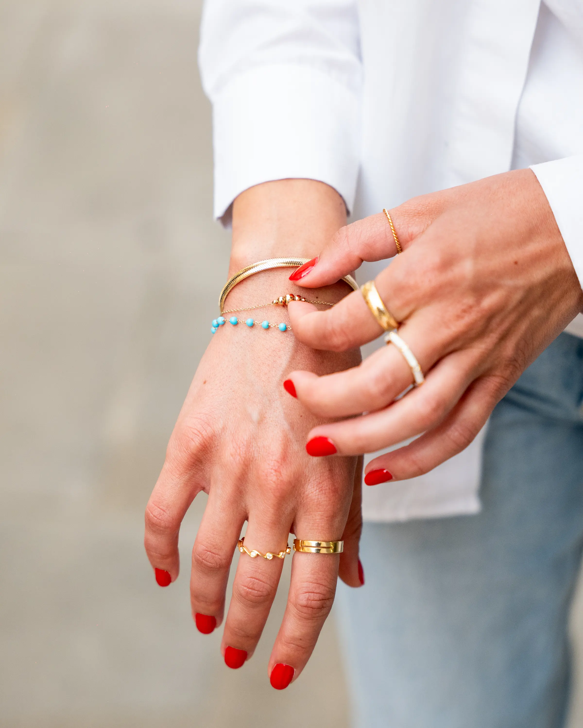 Due mani con bracciali e anelli d’oro sopra un paio di jeans chiari