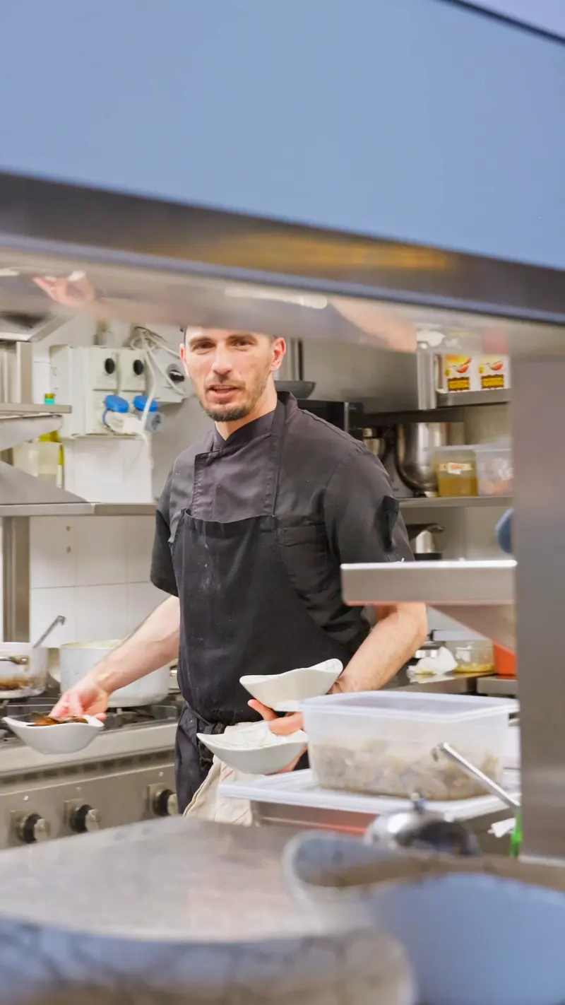 Il cuoco impiatta dietro il banco della cucina