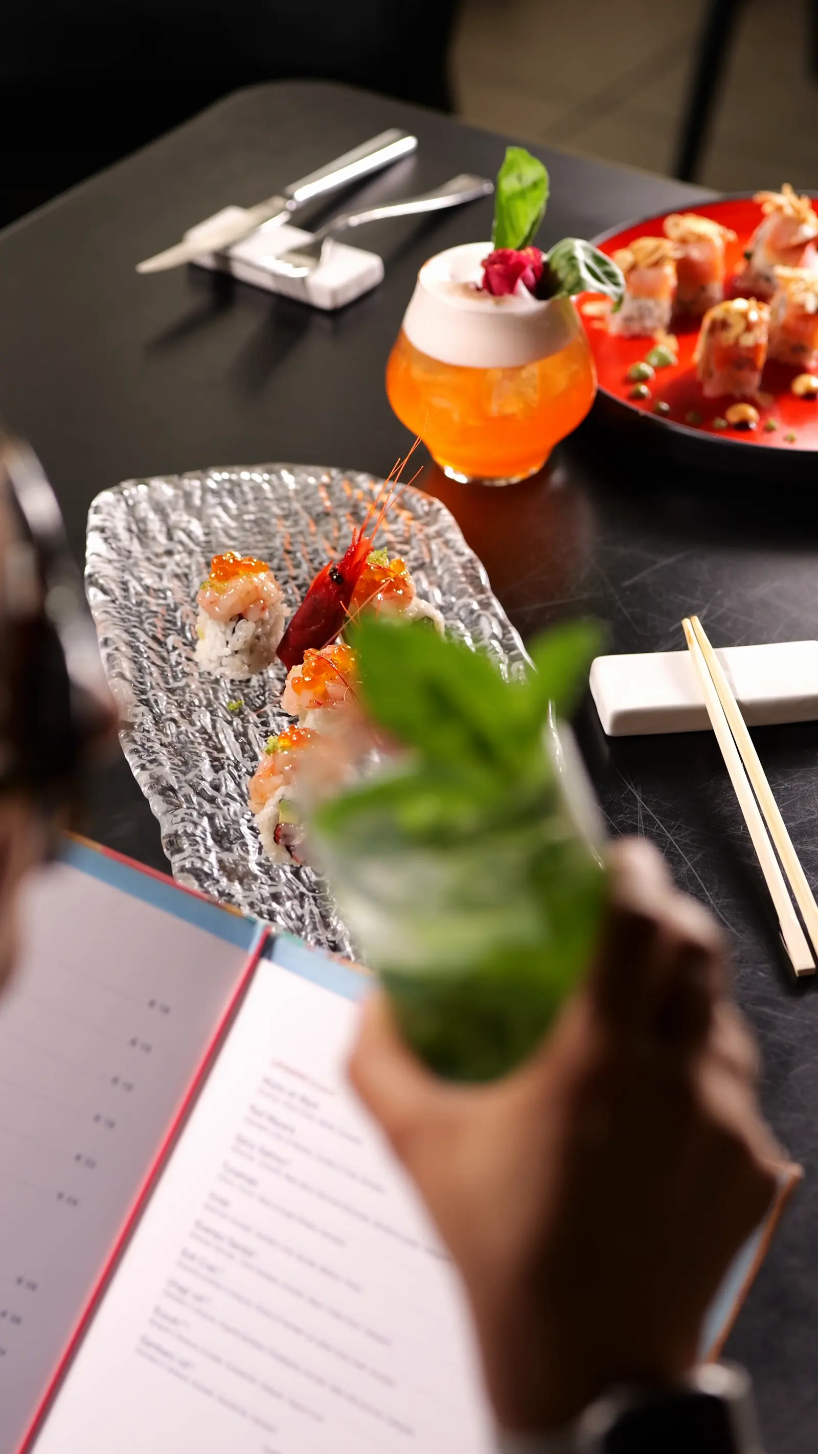 Tavolo con cocktail e crudo di pesce, una mano solleva il bicchiere
