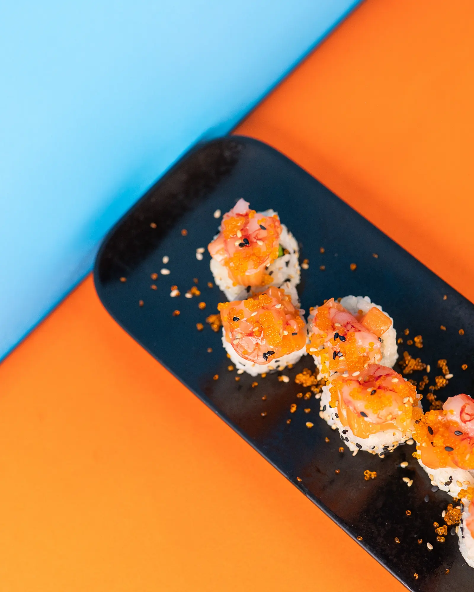 Uramaki al salmone allineati su un vassoio nero, fondo arancione