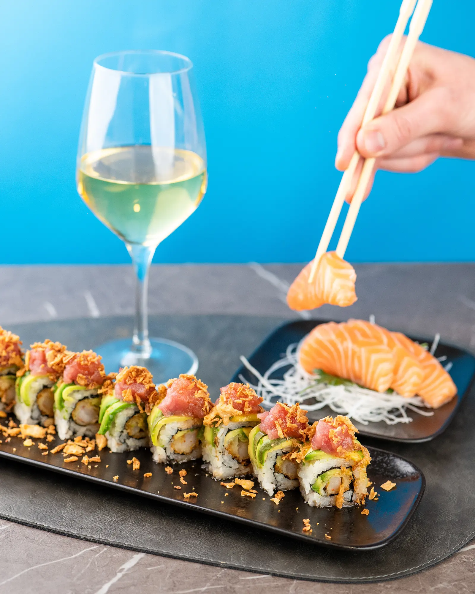 Le bacchette sollevano un pezzo di sushi accanto a un calice di vino bianco