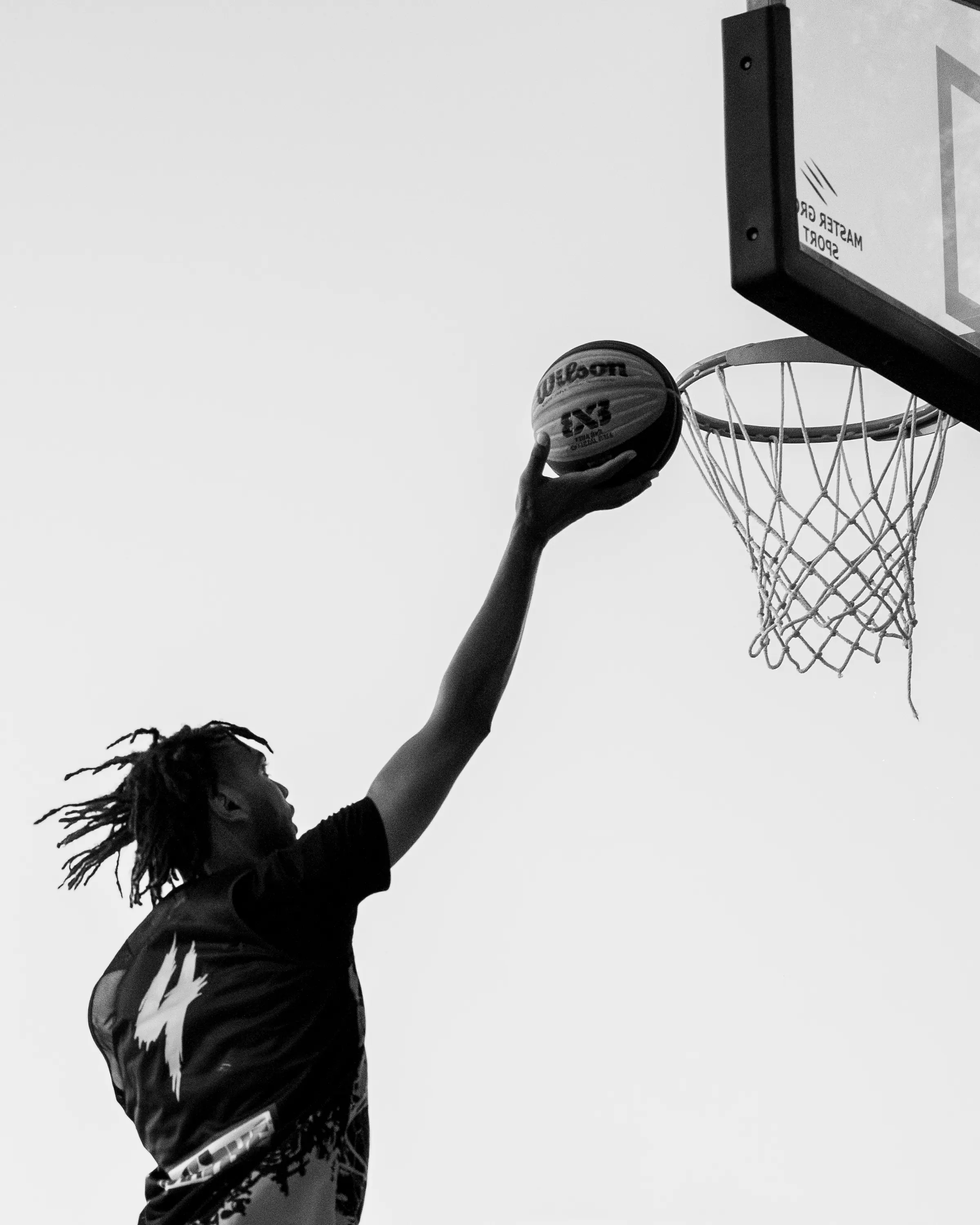 Giocatore con i dreadlocks che appoggia il pallone al ferro, in bianco e nero