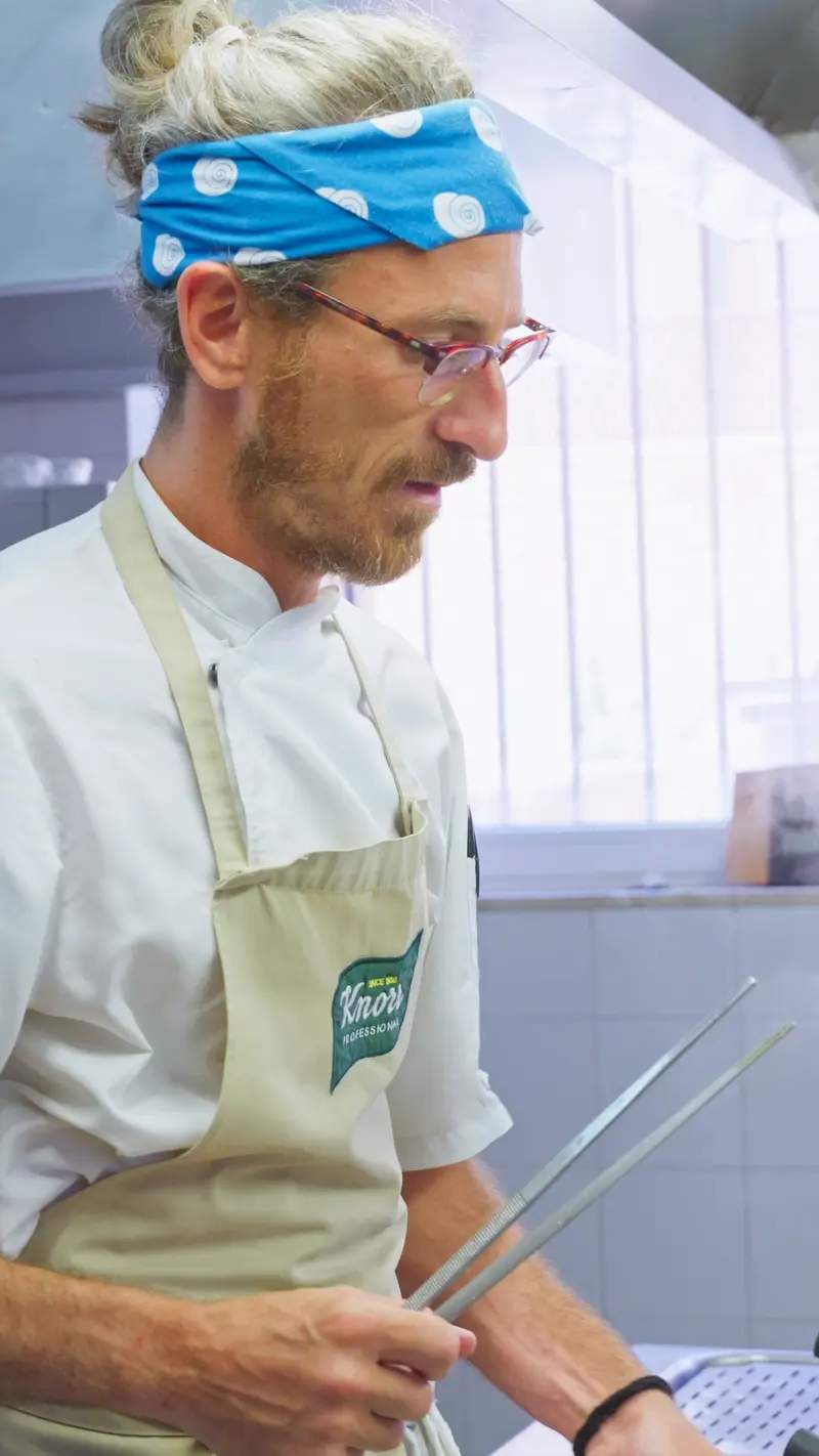 Il cuoco con la bandana lavora dietro il passe della cucina