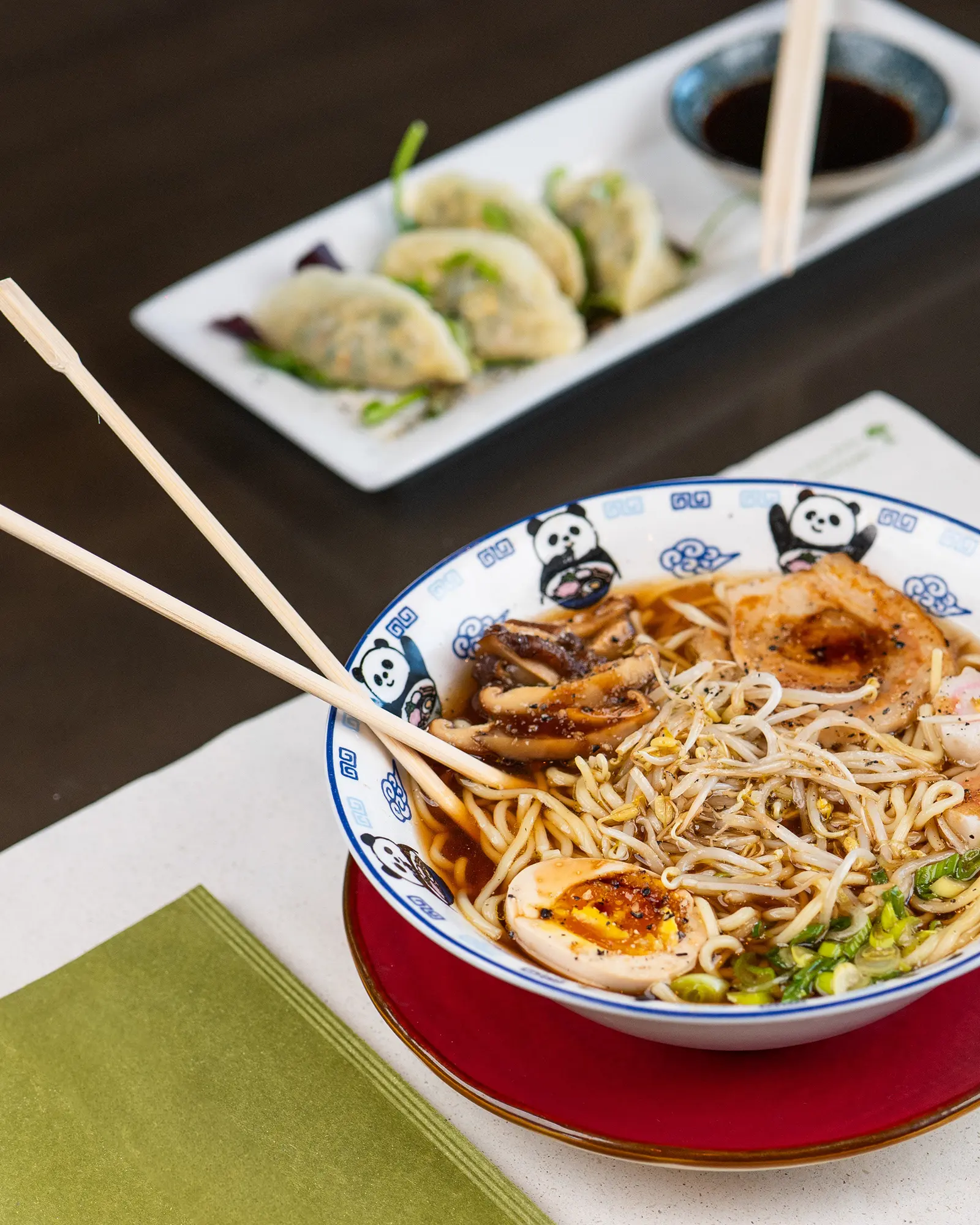 Ramen servito nella ciotola decorata, con il piatto di gyoza dietro