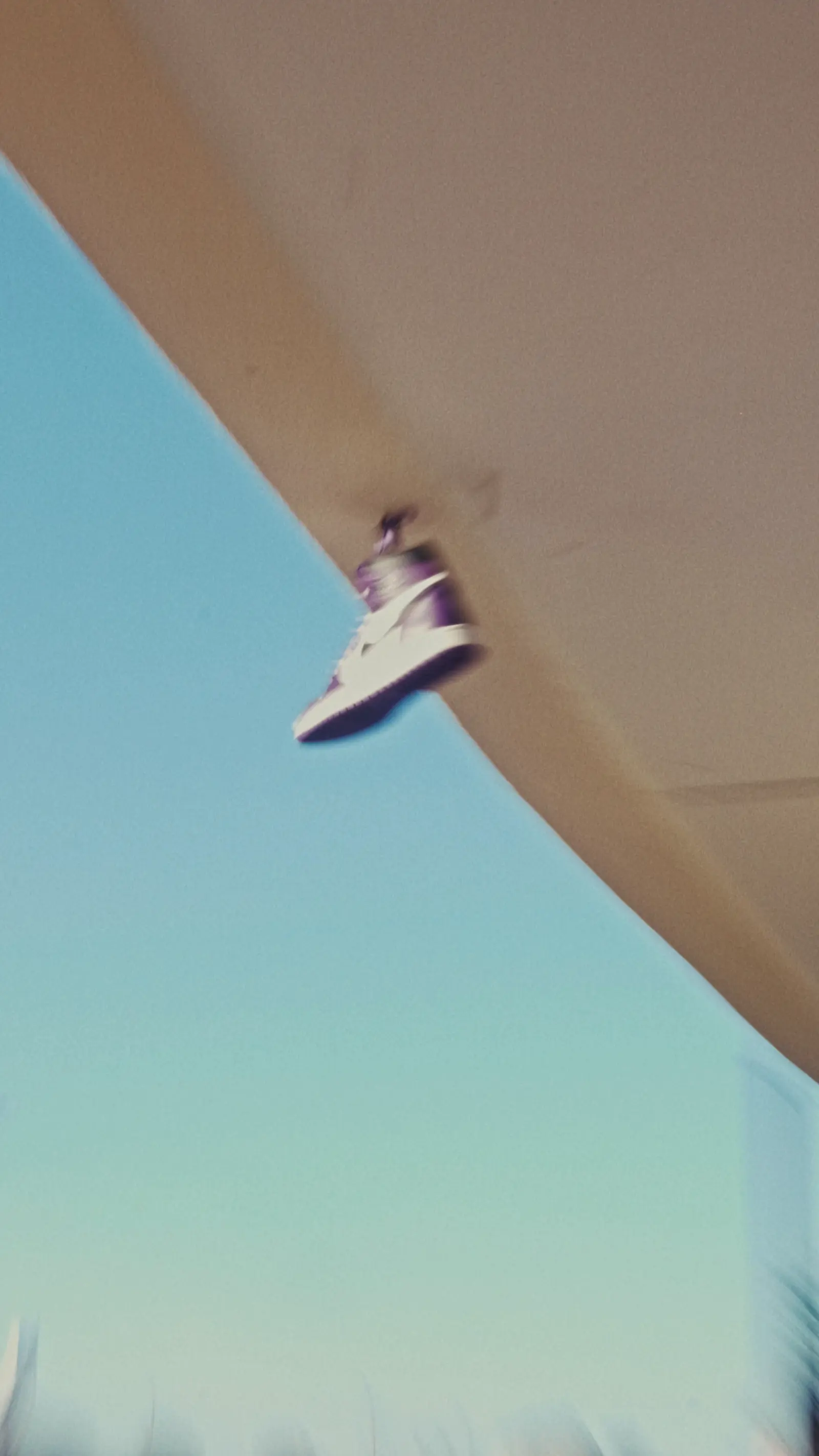 Una sneaker bianca in volo contro il cielo, davanti a un telo chiaro