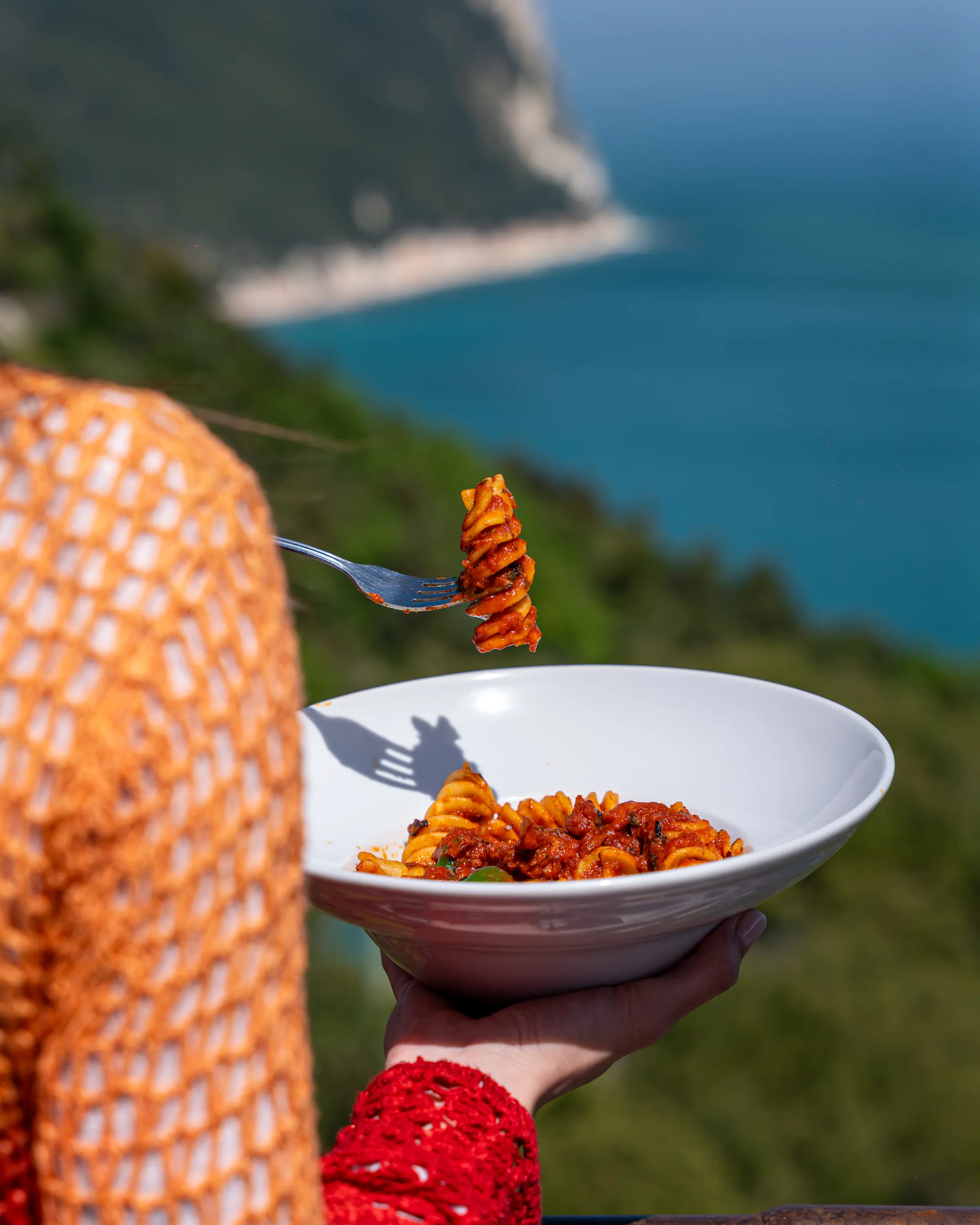 Piatto di pasta tenuto in mano davanti alla baia