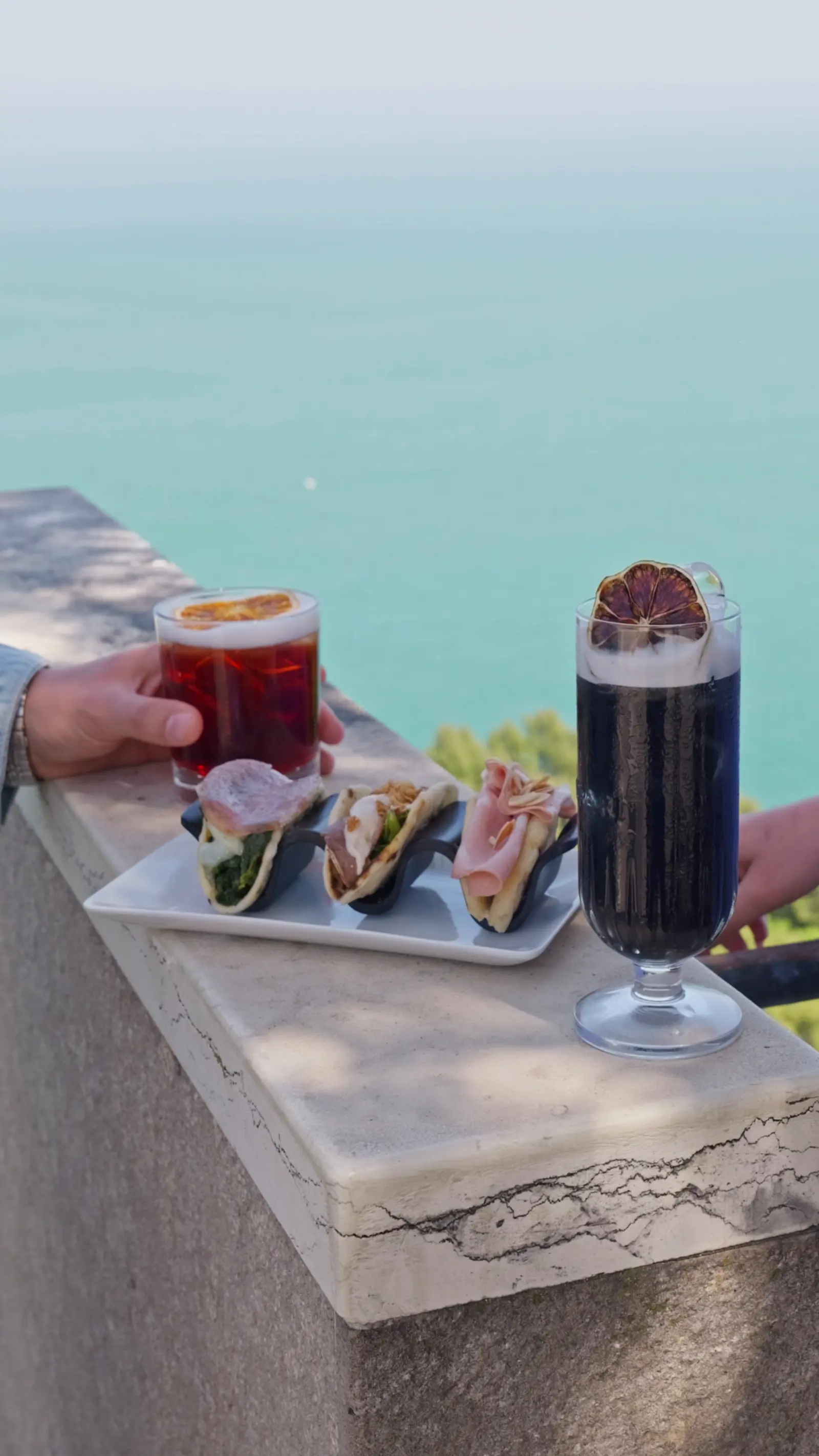 Due drink e un vassoio di piadine sul muretto, con il mare dietro