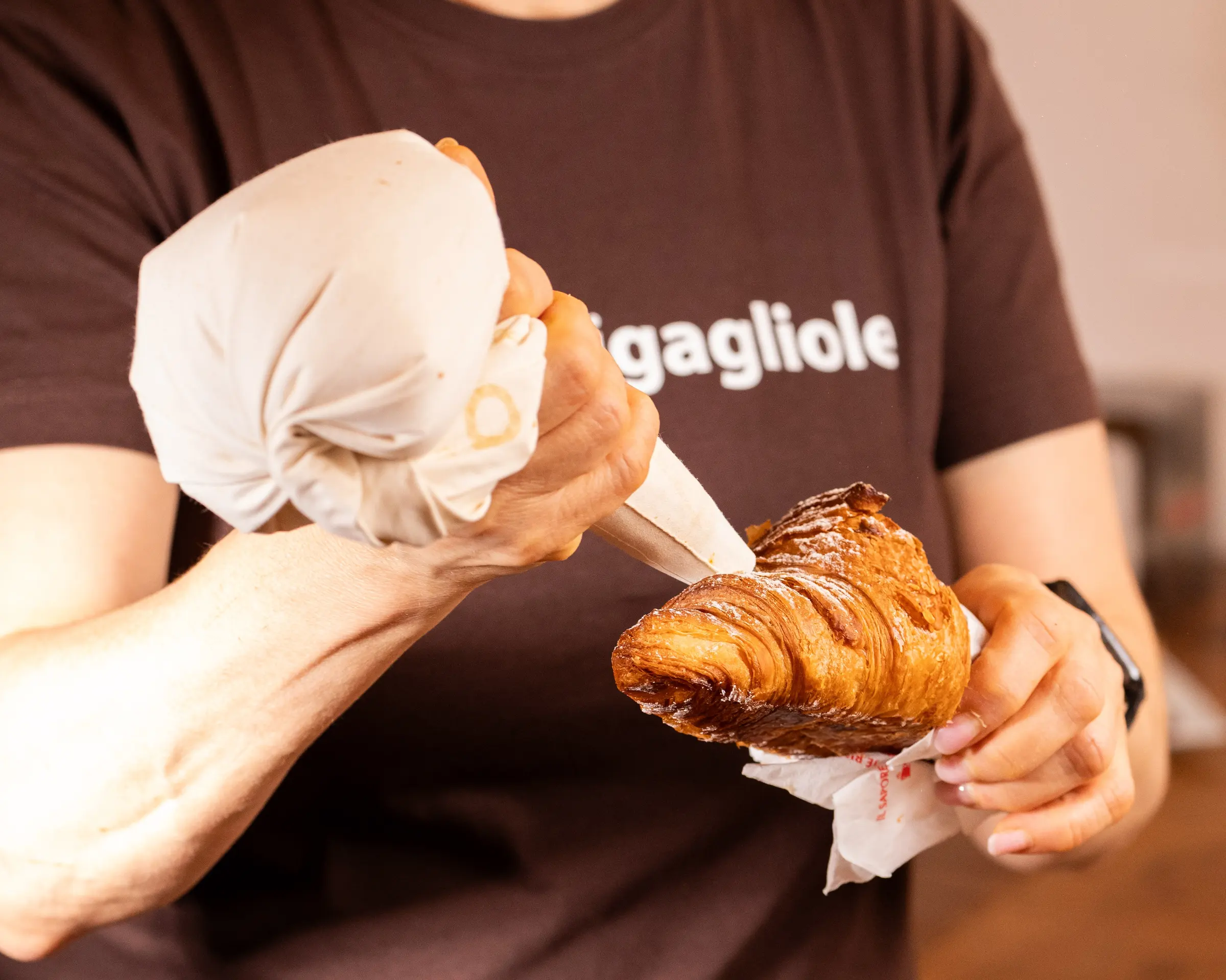 Le mani farciscono un cornetto con la sac à poche, davanti alla maglia del forno