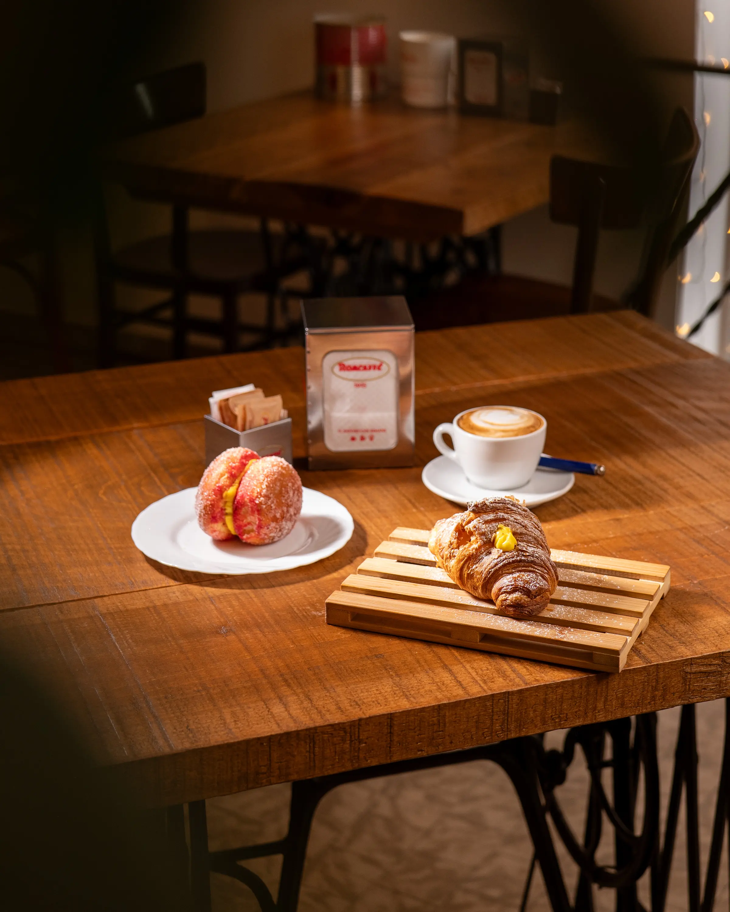 Cappuccino, maritozzo e cornetto sul tagliere, al tavolo del locale