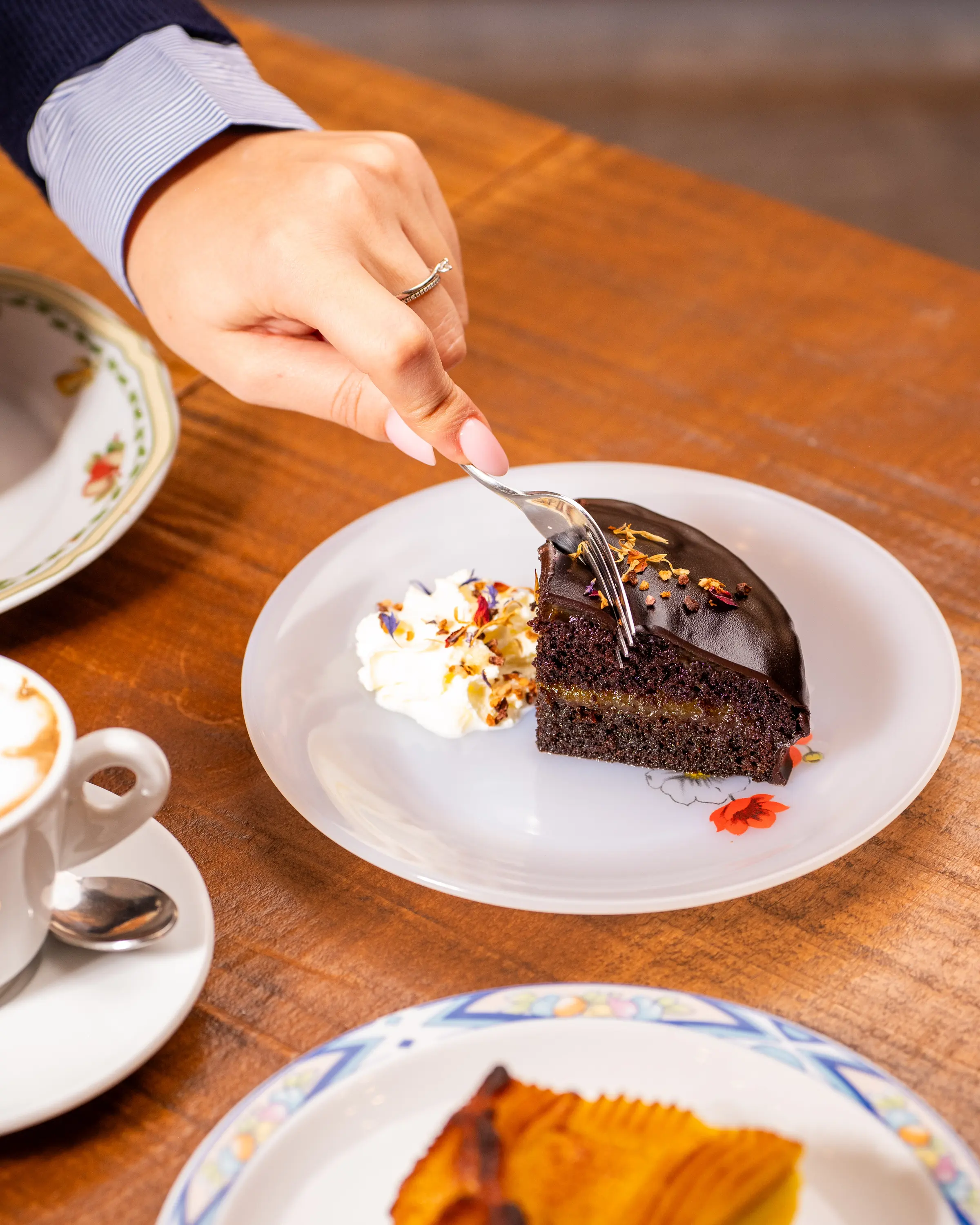 Fetta di torta con panna servita al tavolo, accanto a un cappuccino