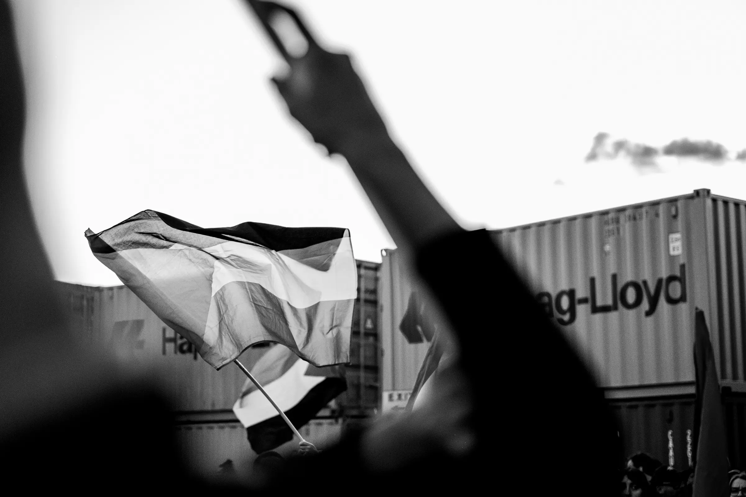Bandiera sventolata davanti ai container del porto, controluce in bianco e nero