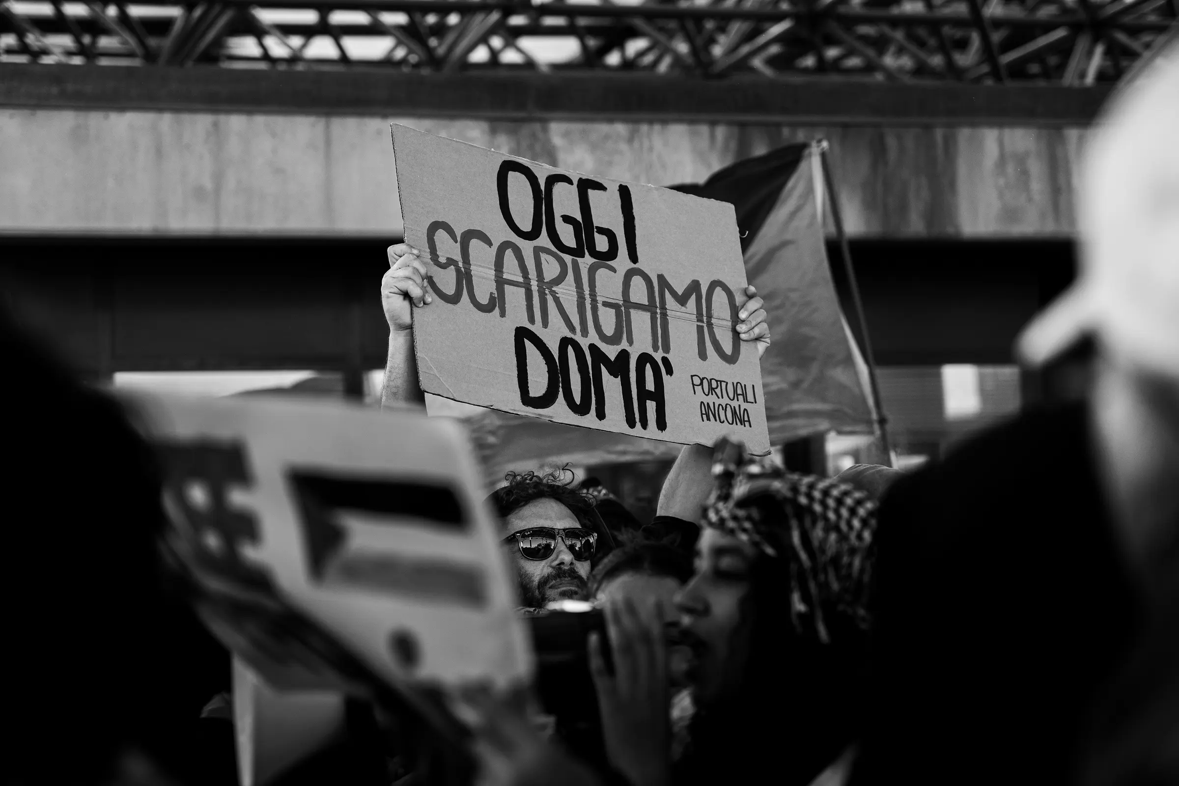 Cartello scritto a mano con la frase «Oggi scarichiamo domà», in bianco e nero