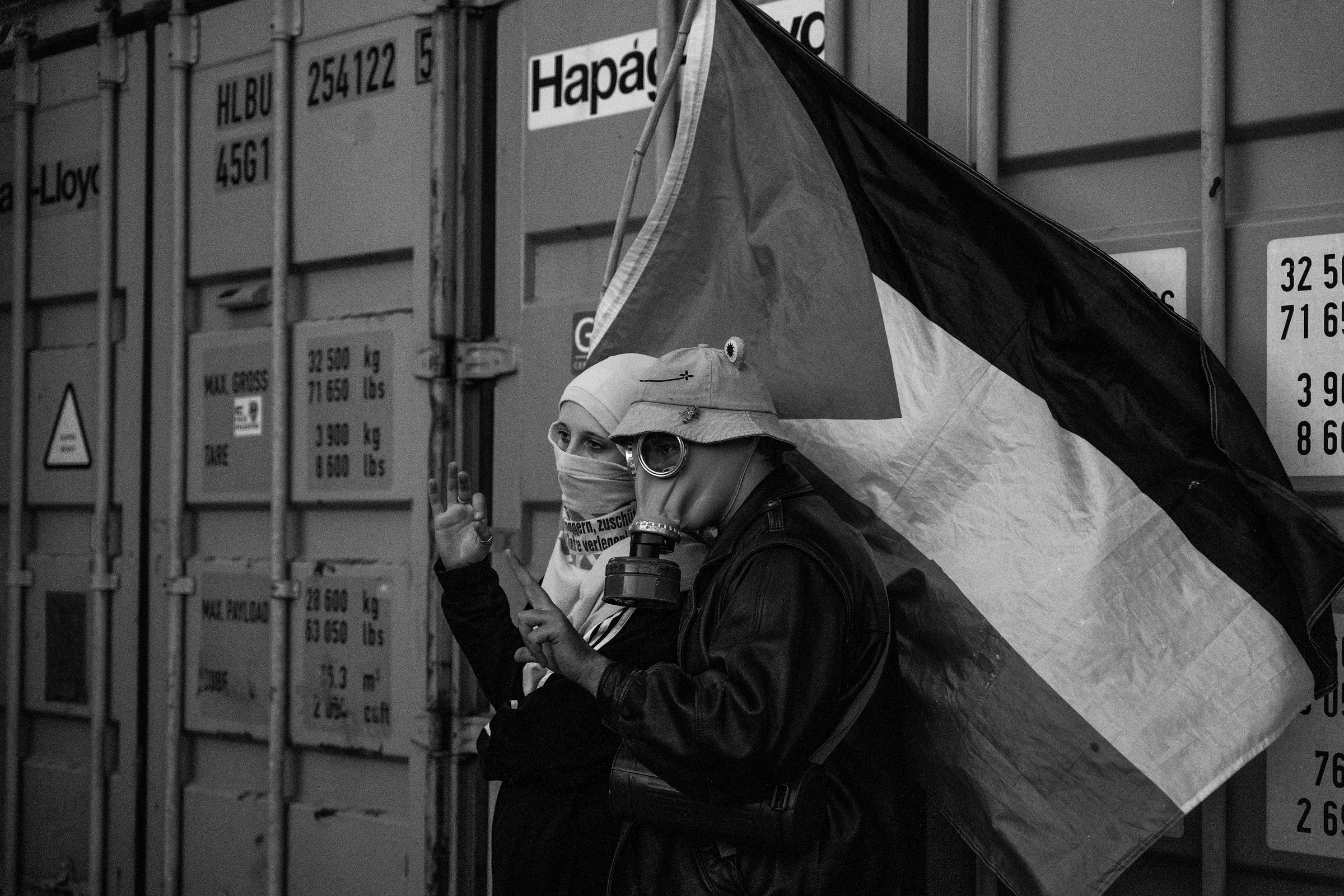 Manifestante con maschera antigas davanti a un container, in bianco e nero