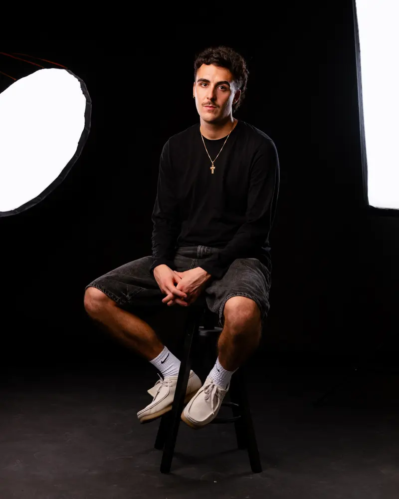 Alessandro Cinti seduto su uno sgabello in studio, su fondo nero