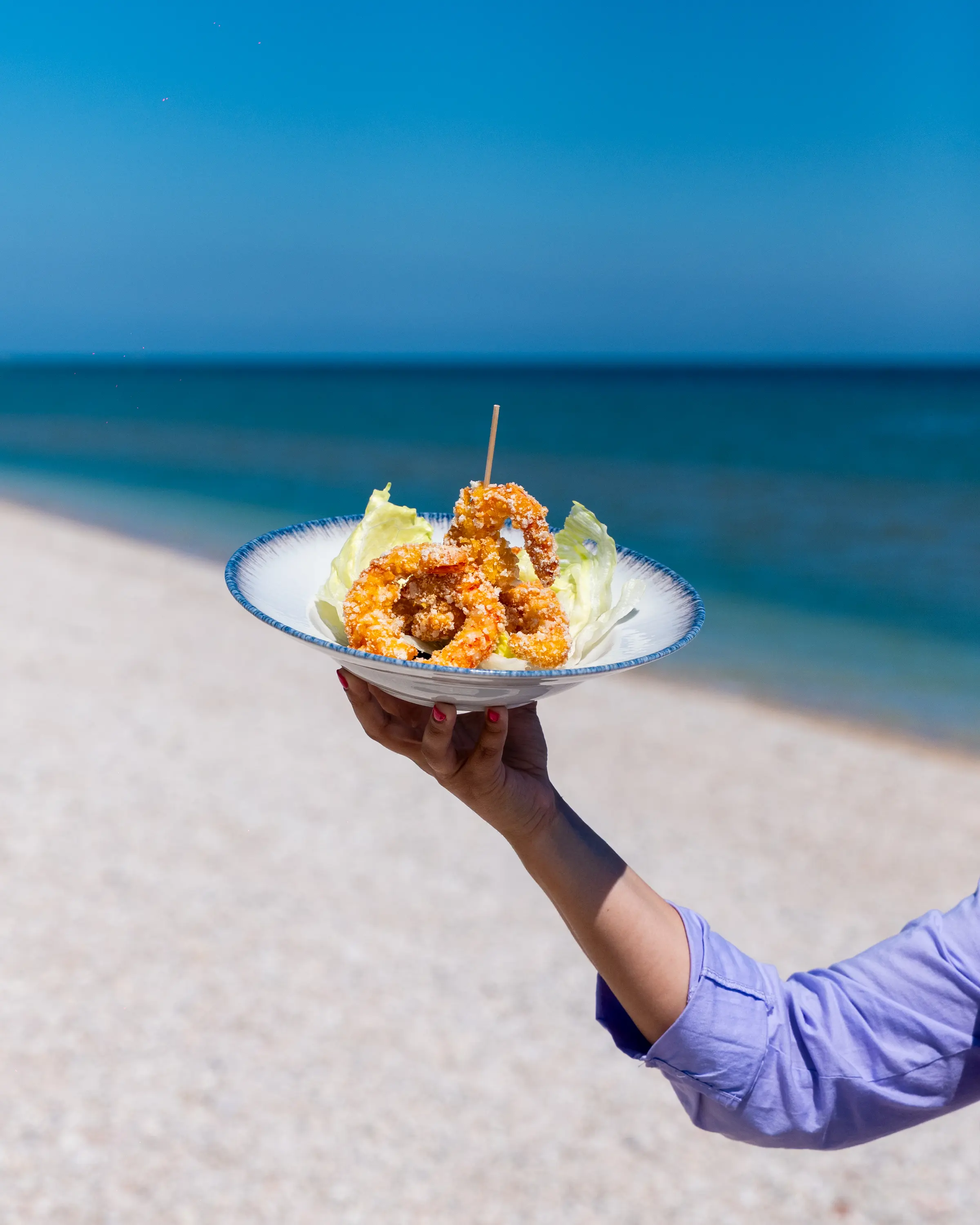 Ciotola di fritto misto tenuta in mano davanti al mare