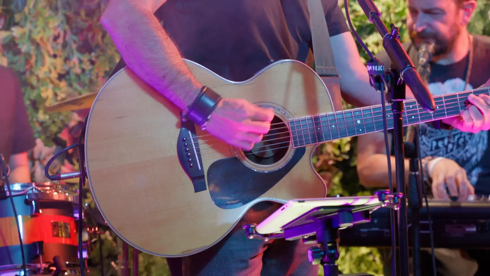 Chitarra acustica suonata dal vivo sotto le luci viola, la batteria accanto