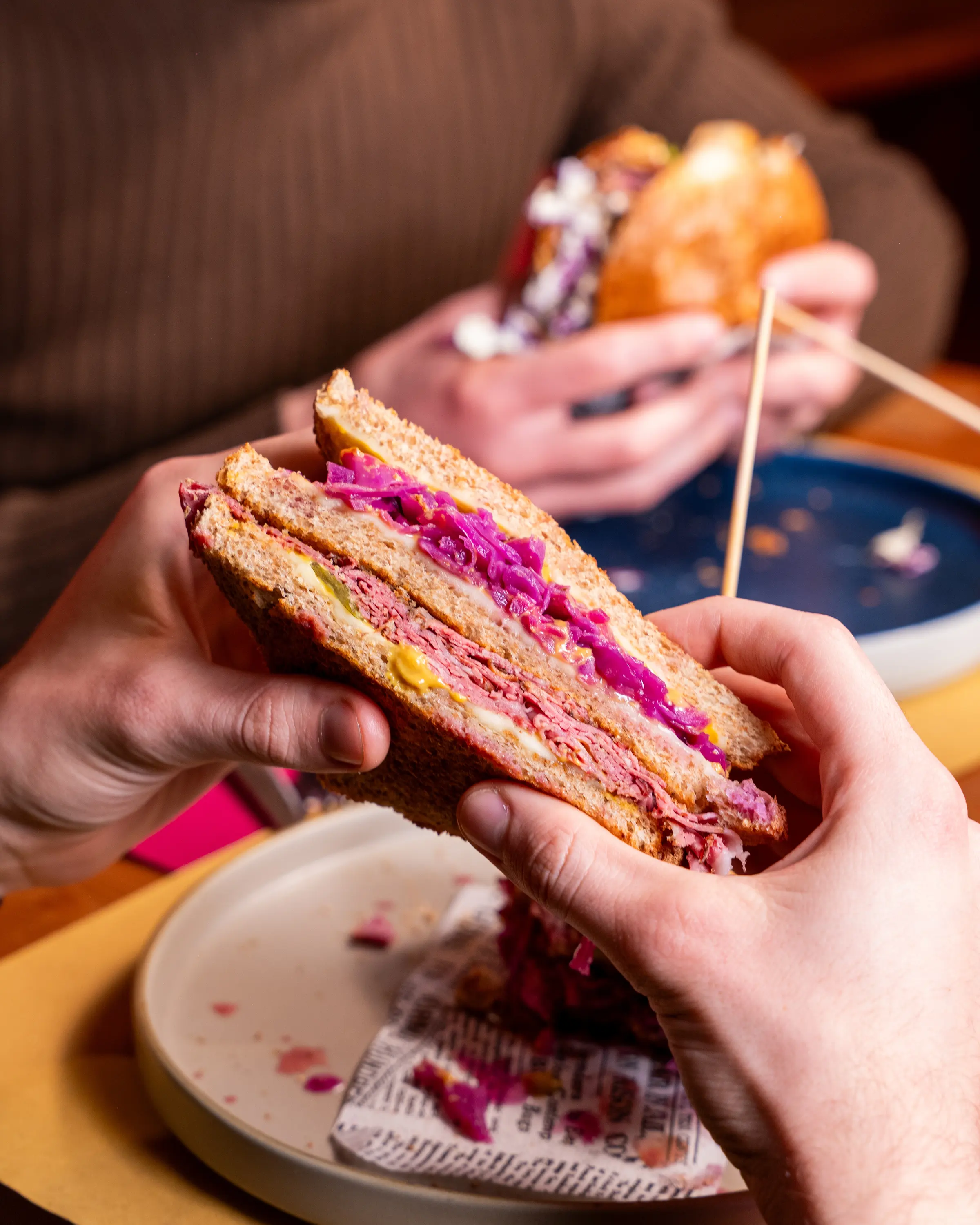 Un panino tagliato a metà tenuto in mano, con pastrami e cavolo viola